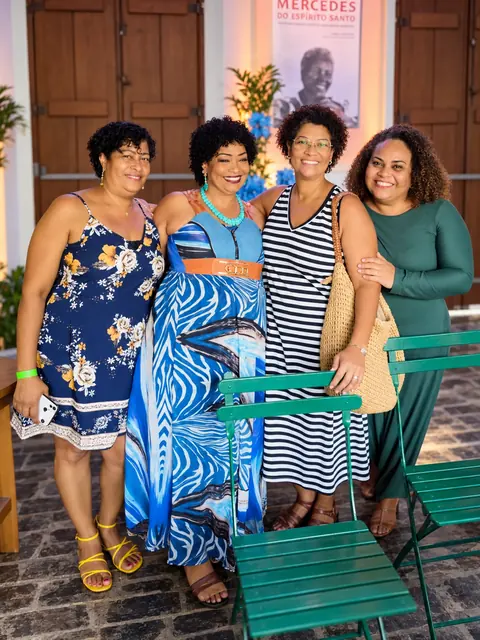 Lícia Viana com três amigas no lançamento do livro, com o banner de Mercedes ao fundo