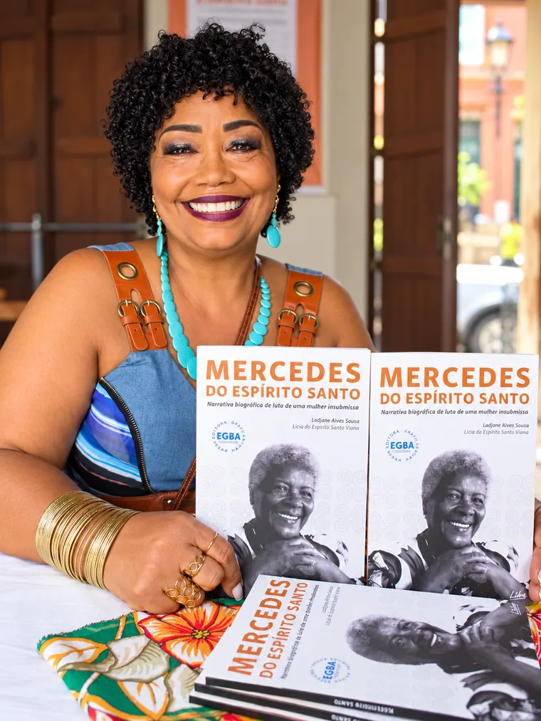 Lícia Viana sorrindo com exemplares do livro Mercedes do Espírito Santo no dia do lançamento